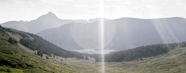 A green mountain valley with peaks silhouetted in the background.